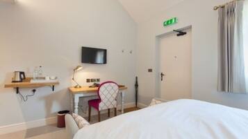 A hotel room with a bed, a desk with a chair, a television, and a door with an emergency exit sign.