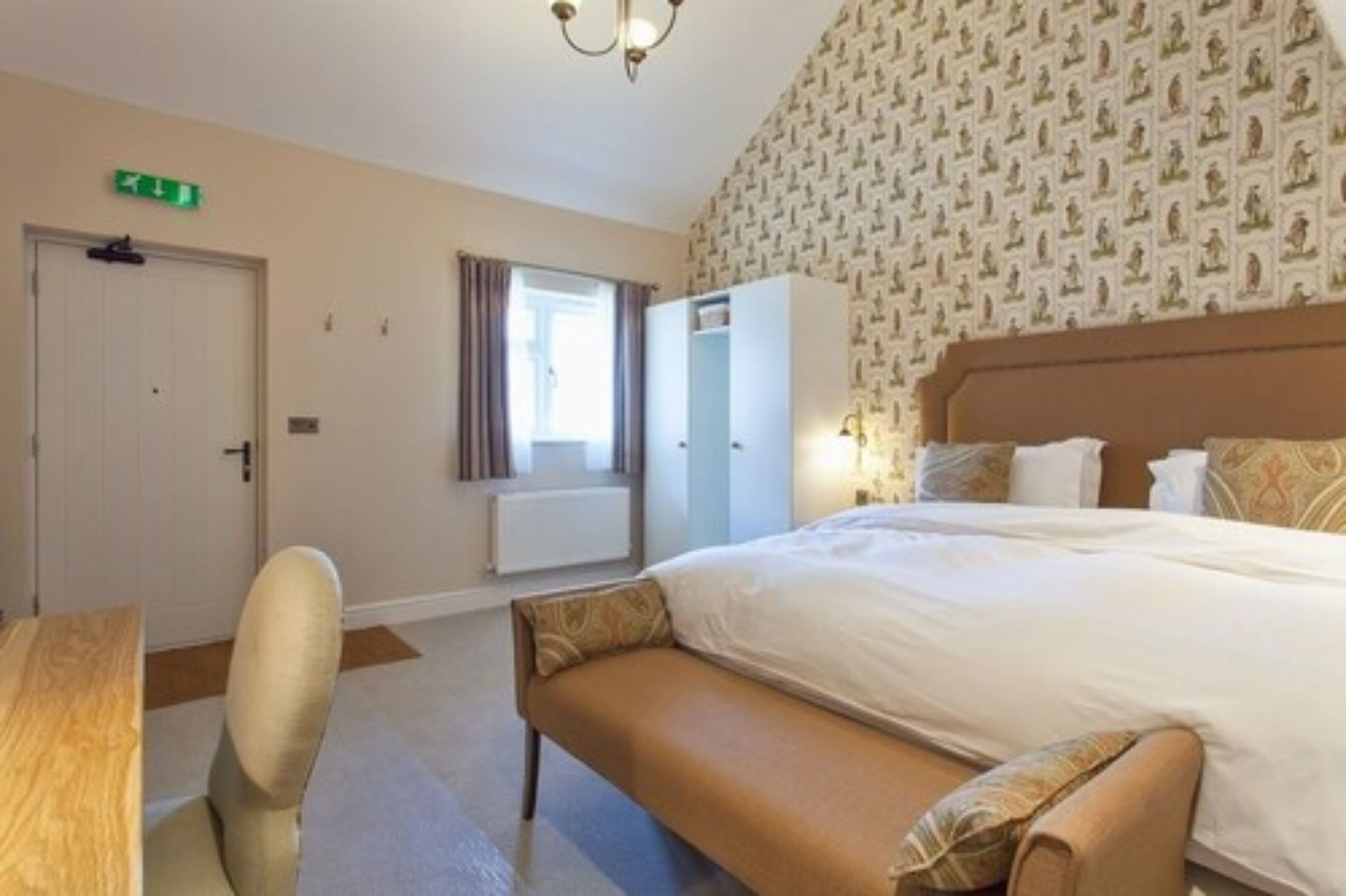 A hotel room with a large bed, a desk, a chair, a wardrobe, and a window with curtains.
