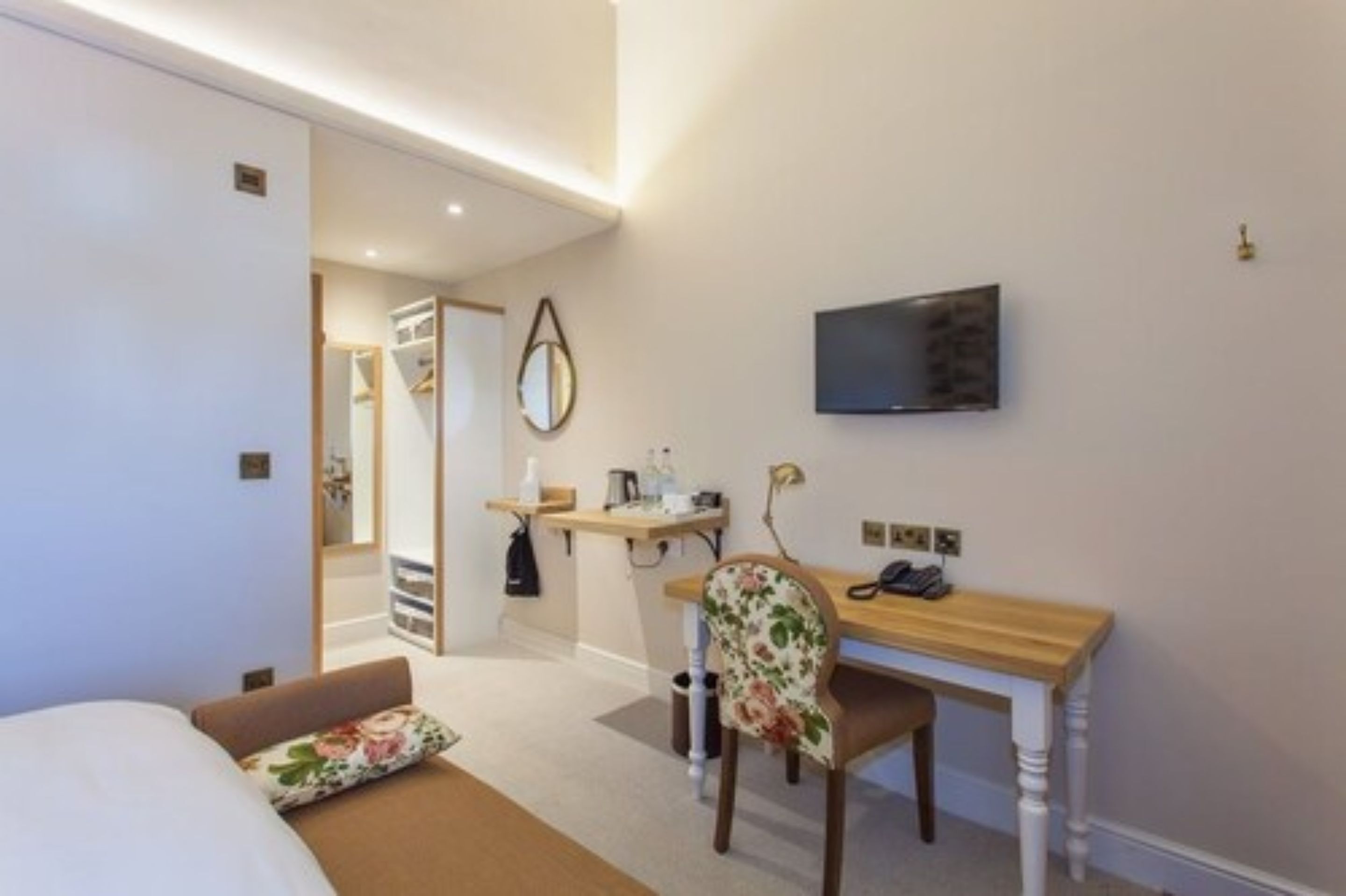 Camera d'albergo con un letto, una scrivania, una sedia, una televisione, uno specchio e uno scaffale con articoli da toilette.