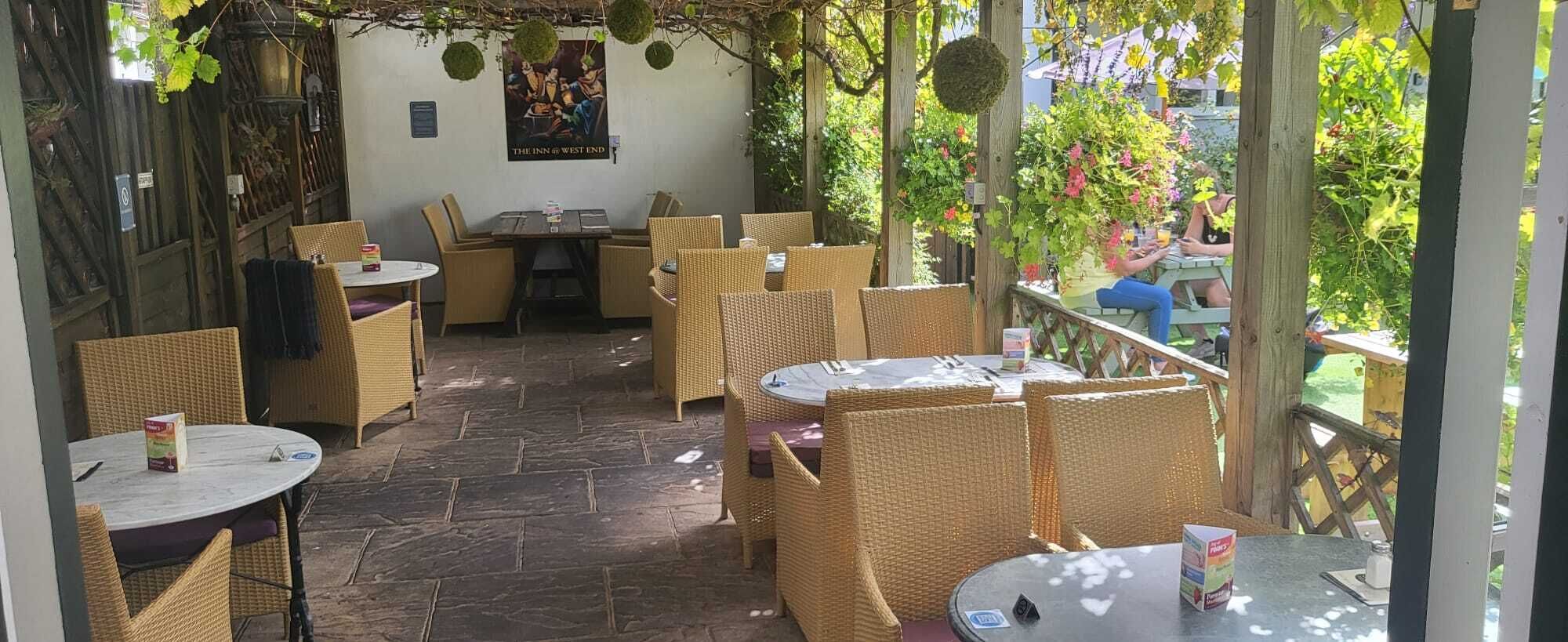 An outdoor patio area with wicker furniture and stone flooring, featuring a poster on the wall and a view of a garden.