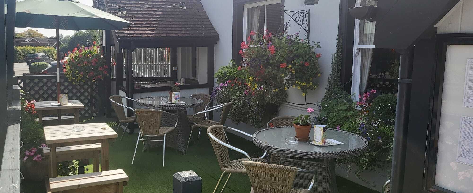 Un patio al aire libre con mobiliario de mimbre, una mesa redonda y plantas en macetas.