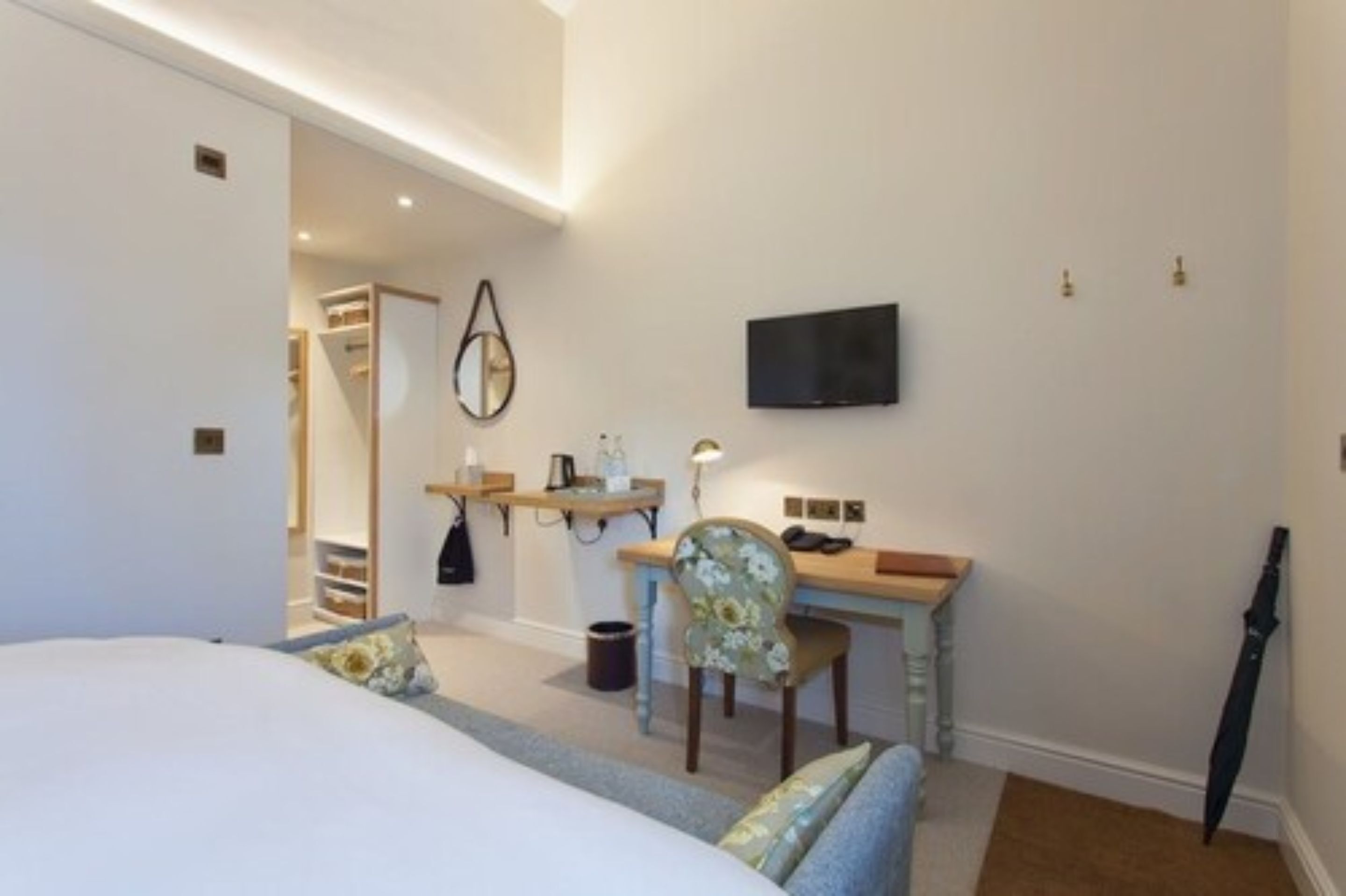 A hotel room with a bed, a desk with a chair, a TV mounted on the wall, and a coat rack.