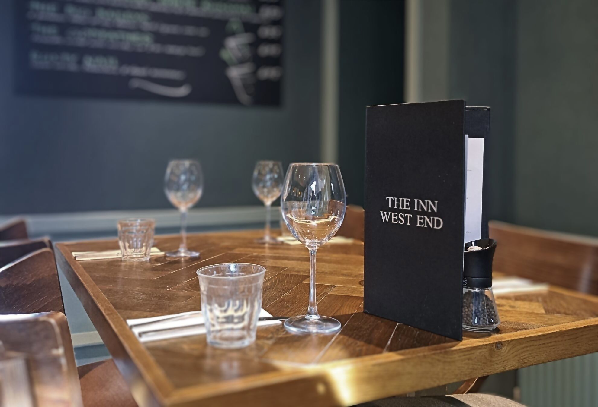 A table set with glasses and a menu stand labeled "THE INN WEST END".