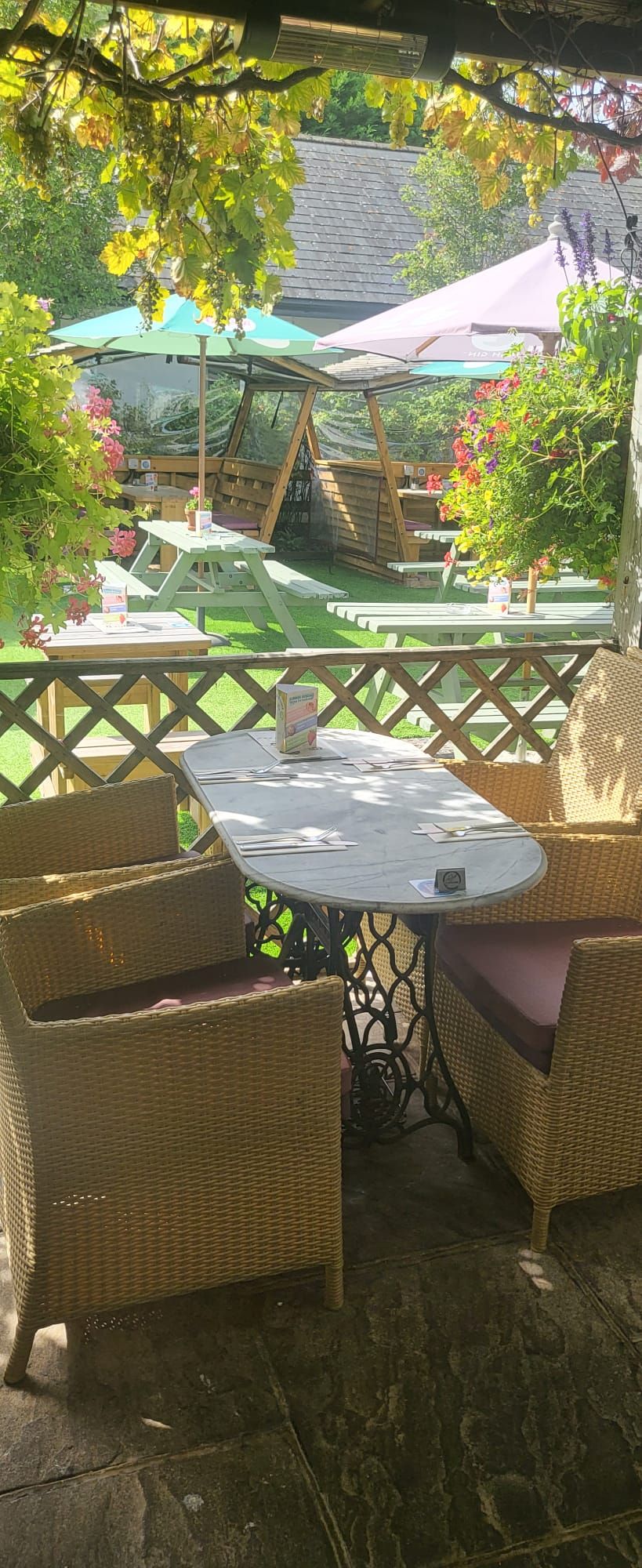 Un espacio al aire libre con mobiliario de mimbre y una mesa, rodeado por una valla de madera y follaje.