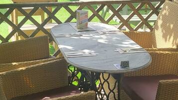 Un espacio al aire libre con mobiliario de mimbre y una mesa, rodeado por una valla de madera y follaje.
