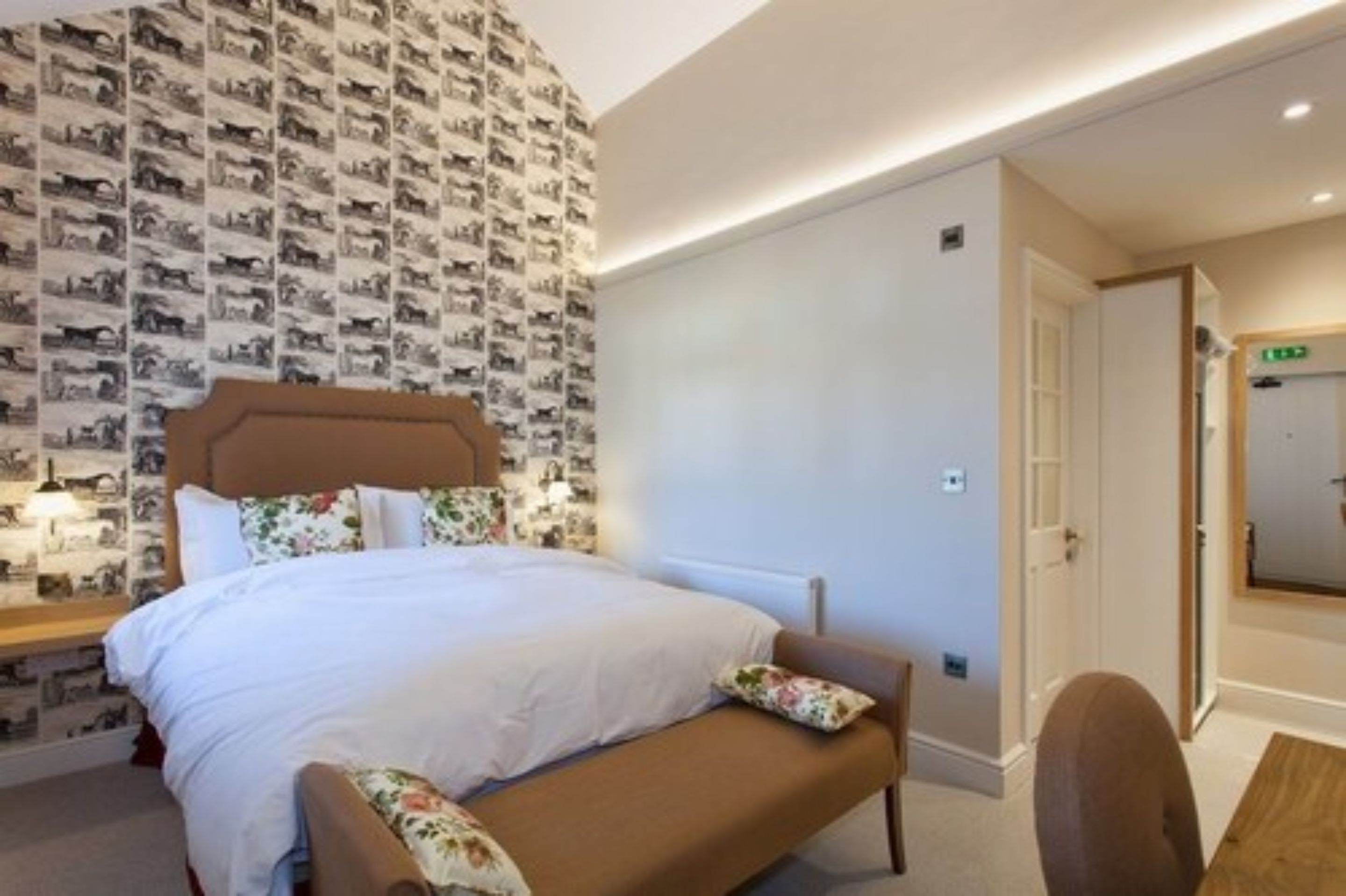 A bedroom with a bed, a bench, a bedside table, and a wall with a repeating pattern.