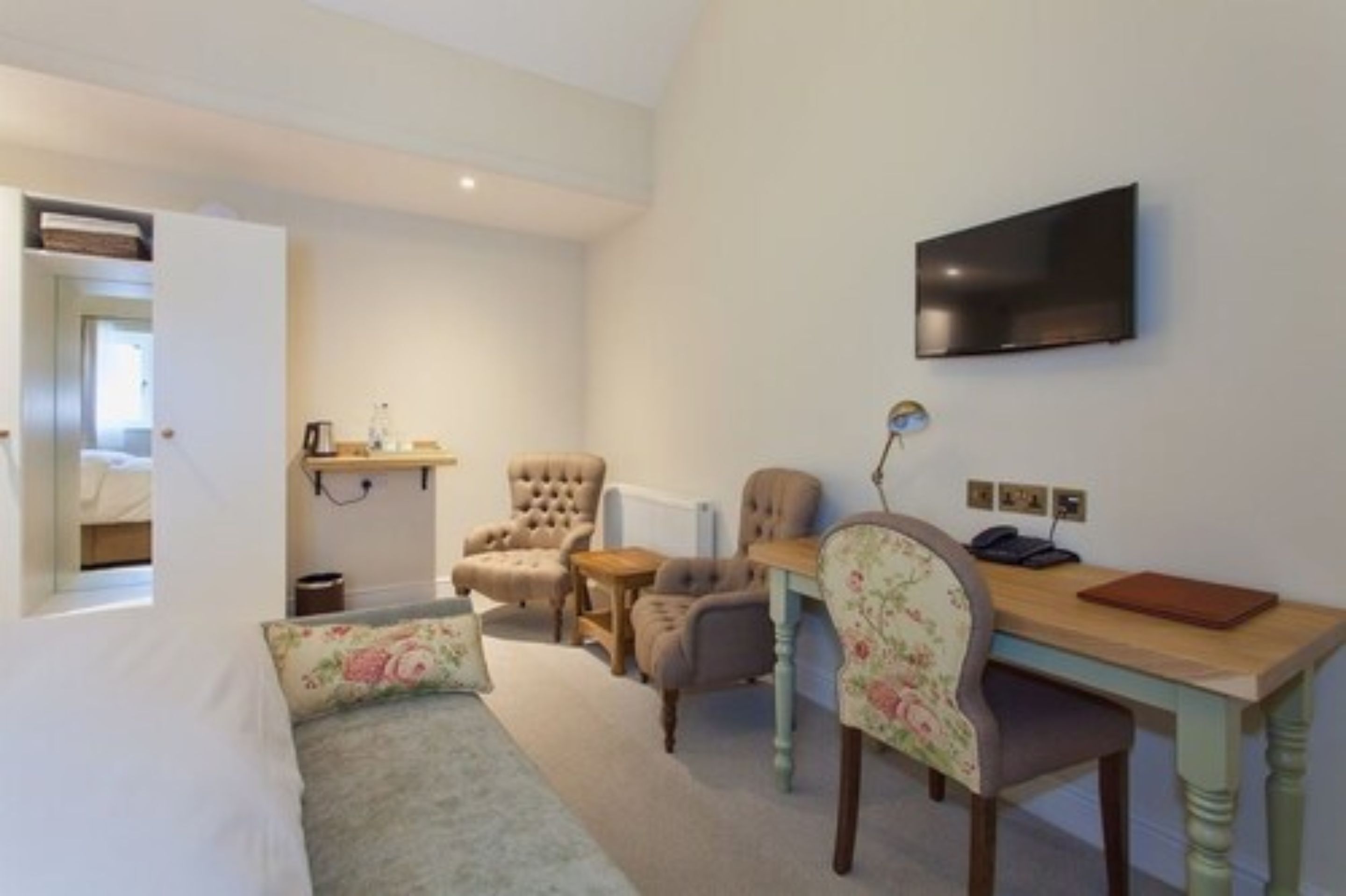 A bedroom with a bed, a desk, two chairs, a television, and a small shelf with items.