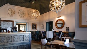 A restaurant interior with wooden bar counters, multiple seating areas, and decorative lighting fixtures. - The Inn West End (Woking)