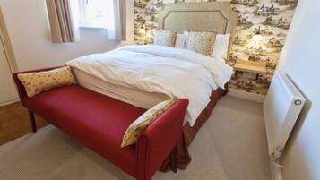 Un dormitorio con una cama, un banco rojo, una mesita de noche y un radiador.