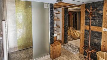 Une salle de bain moderne avec une douche à l’italienne en verre, un meuble-lavabo en bois et un mur en pierre.