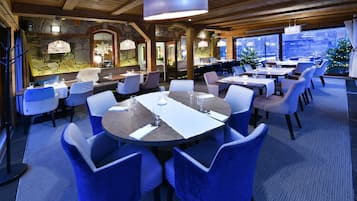 Un restaurante con mesas redondas y sillas azules, paredes de piedra y vistas al exterior.