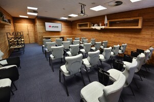 Un salón de conferencias con filas de sillas, una pantalla de proyector y paredes de madera.
