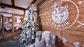 A cozy interior with a Christmas tree, plaid furniture, and a wooden wall with a logo. - APLEND Hotel Kukučka a Rezidencie (Vysoké Tatry)