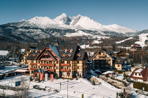 A large, traditional chalet-style hotel with multiple balconies and a ski slope in the background.
