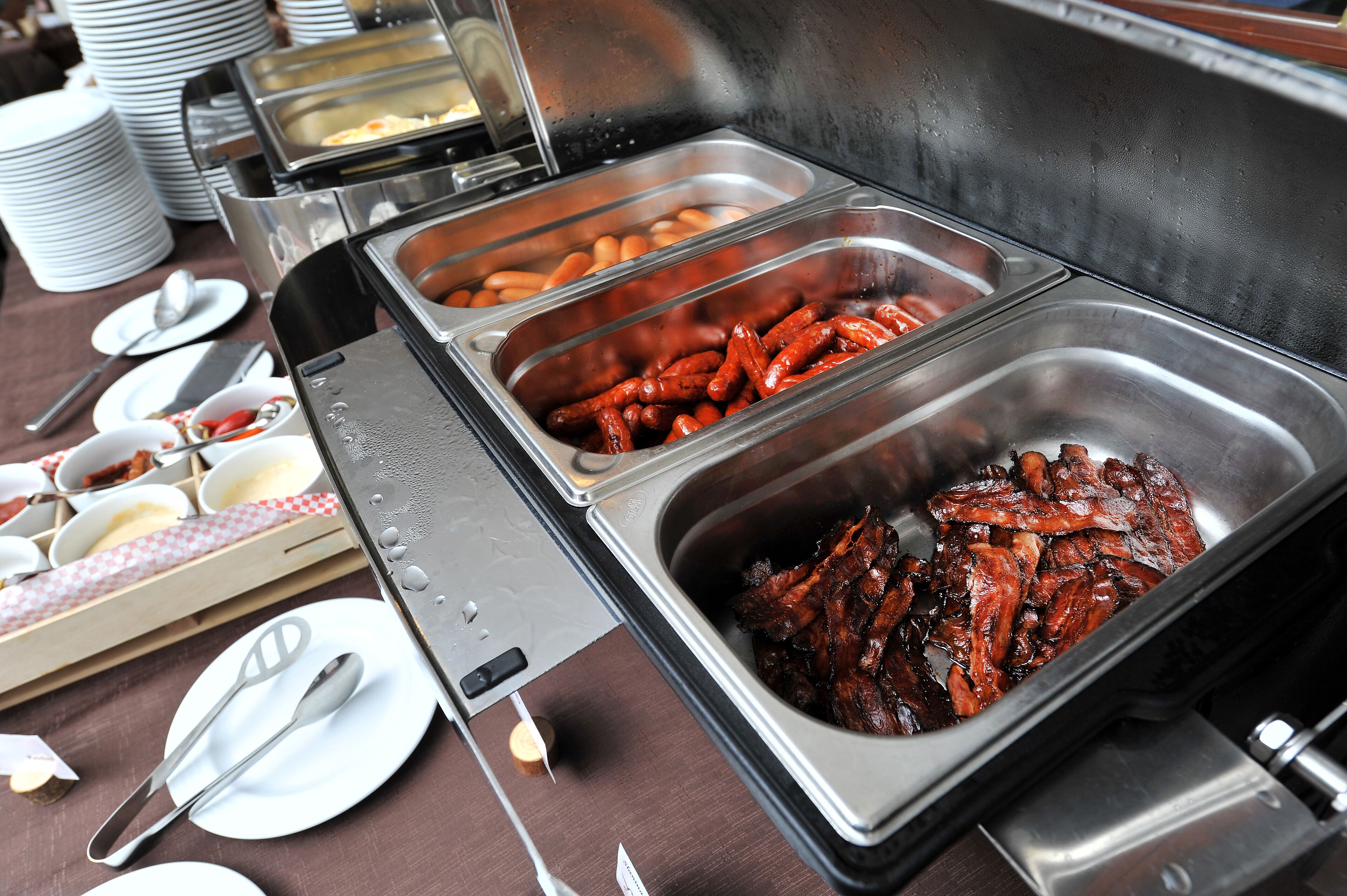 Ein Buffet mit verschiedenen Speisen, darunter Würstchen und andere Fleischgerichte, serviert in Metallbehältern.