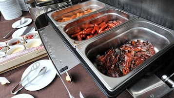 Ein Buffet mit verschiedenen Speisen, darunter Würstchen und andere Fleischgerichte, serviert in Metallbehältern.