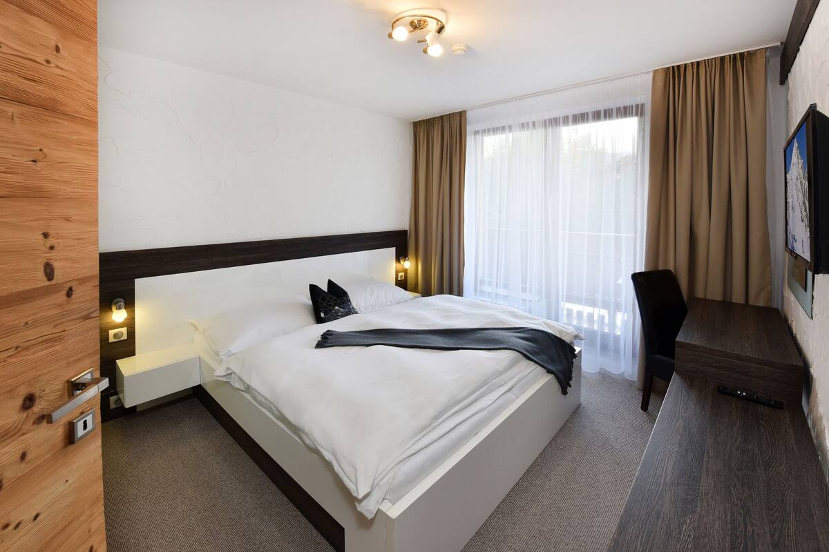 A hotel room with a bed, bedside table, and a desk with a chair.