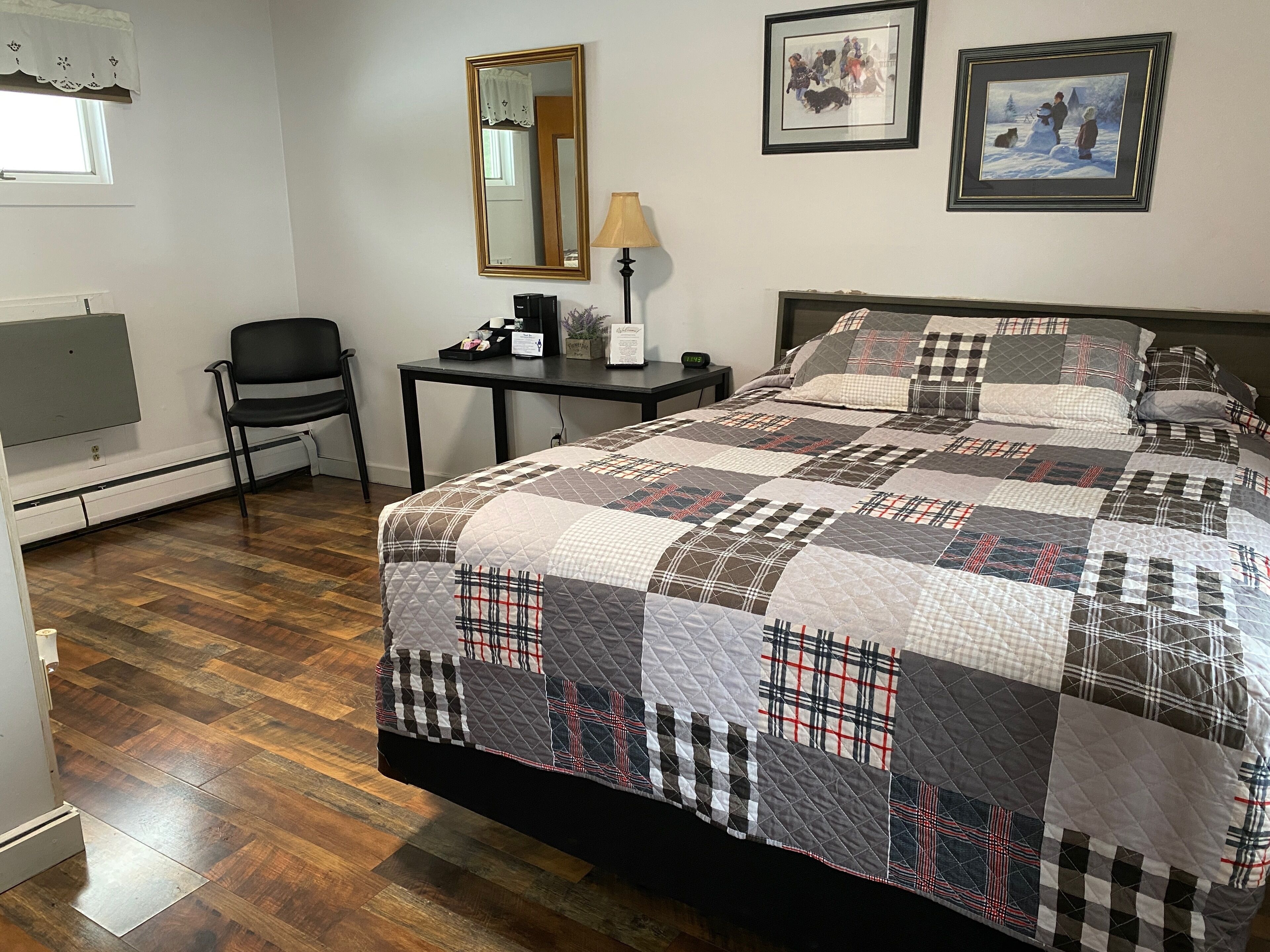 A bedroom with a large bed, a desk, a chair, a mirror, and two framed pictures on the wall.