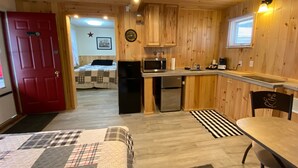 A cozy cabin-style room with a kitchenette, a dining area, and a bed with a checkered quilt. - Northern Family Motel (Potsdam)
