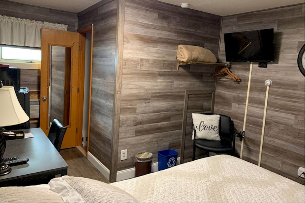 A hotel room with a bed, a desk with a lamp, a chair, a television mounted on the wall, and a wooden accent wall.