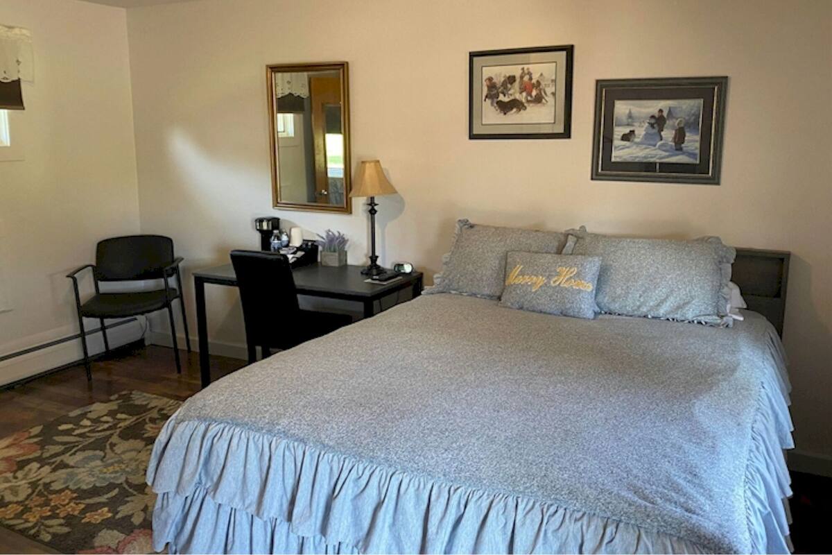 A hotel room with a bed, a desk, a chair, a lamp, and two framed pictures on the wall.