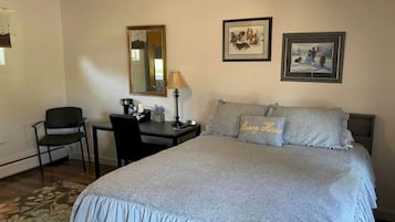 Una camera d'albergo con un letto, una scrivania, una sedia, una lampada e due quadri appesi al muro.