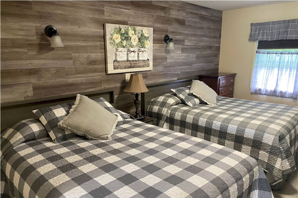 A room with two beds, a wooden headboard, a painting, and a window with curtains.