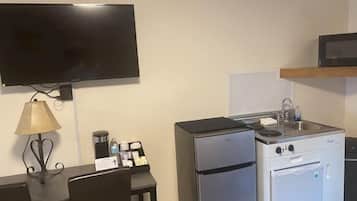 Una kitchenette compacta con refrigerador, estufa, microondas y un televisor de pantalla plana montado en la pared.