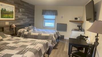 A bedroom with two beds, a desk, a chair, a TV, and a window with a view of the outdoors.