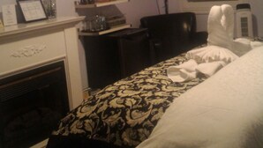 Una camera d'albergo con un letto, una scrivania, una televisione, un camino e una finestra con persiane.