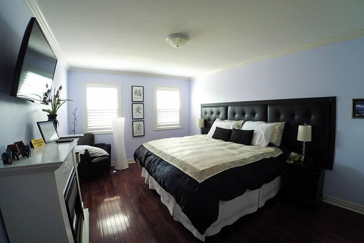 A bedroom with a large bed, a desk, a chair, and a television on the wall.