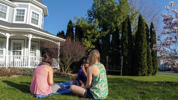 Three people sitting on the grass in front of a house with a porch and a tree with pink blossoms.