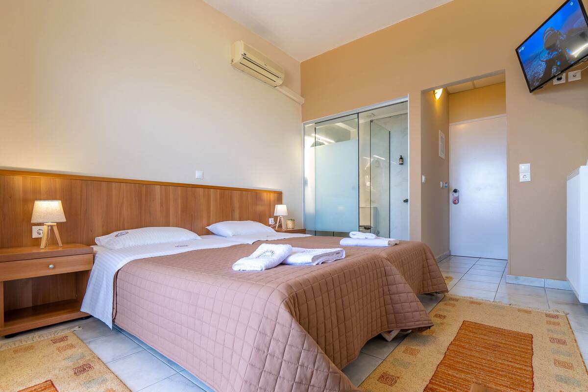 A hotel room with a bed, bedside tables, a TV, and a bathroom with a glass door.