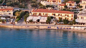 A coastal hotel with multiple buildings, a beach with sun loungers, and a view of the sea. - Sunset Hotel (North Kynouria)