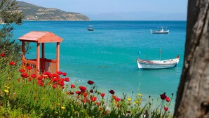 A coastal scene with a wooden gazebo, boats, and a clear blue sea. - Sunset Hotel (North Kynouria)