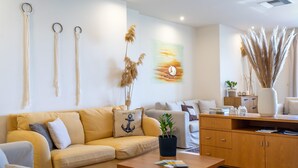 A modern living room with a sofa, coffee table, and a cabinet. There are decorative plants and a painting on the wall. - Sunset Hotel (North Kynouria)