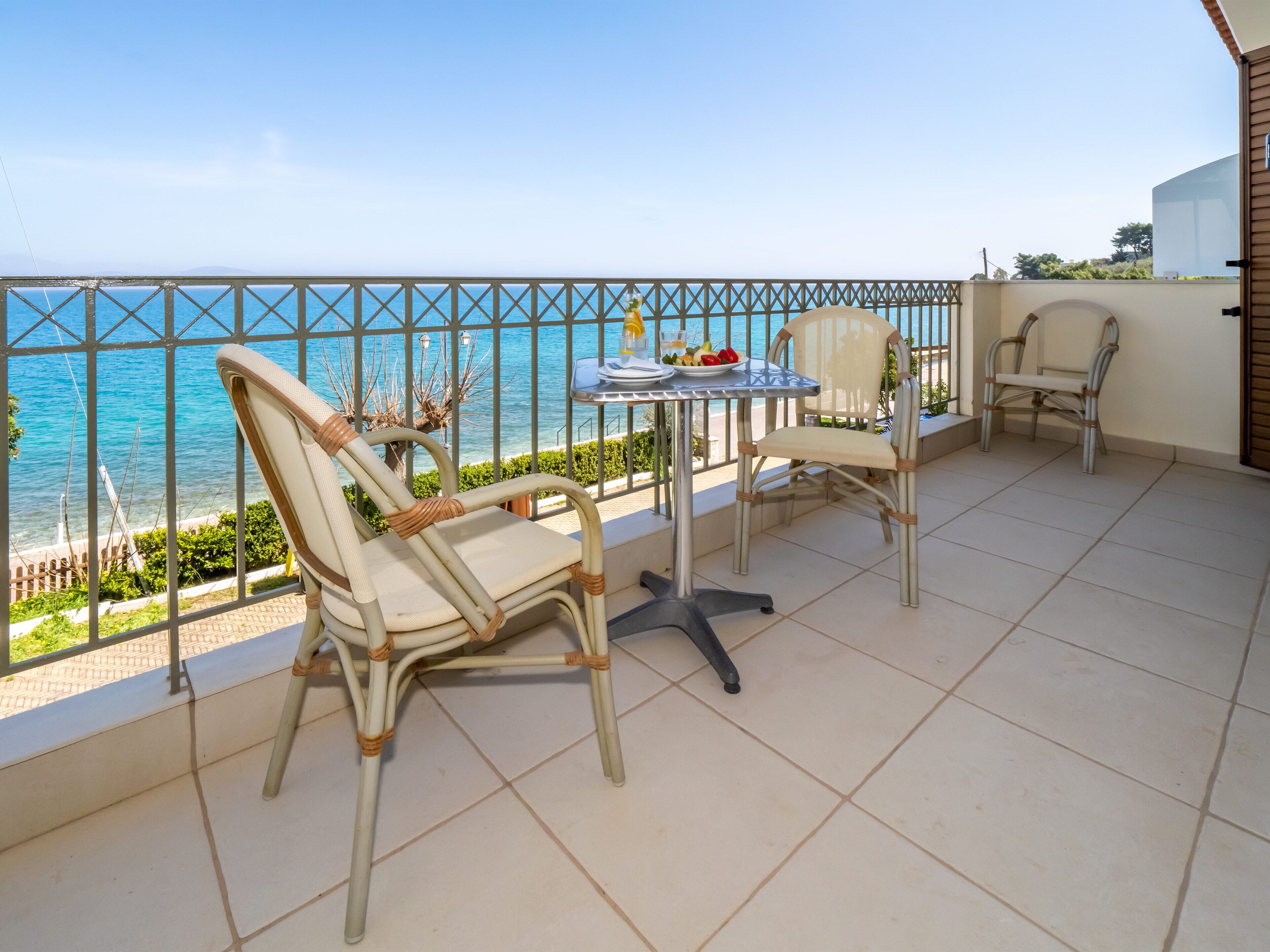 Un balcon avec deux fauteuils en osier et une petite table, donnant sur une mer d’un bleu limpide.