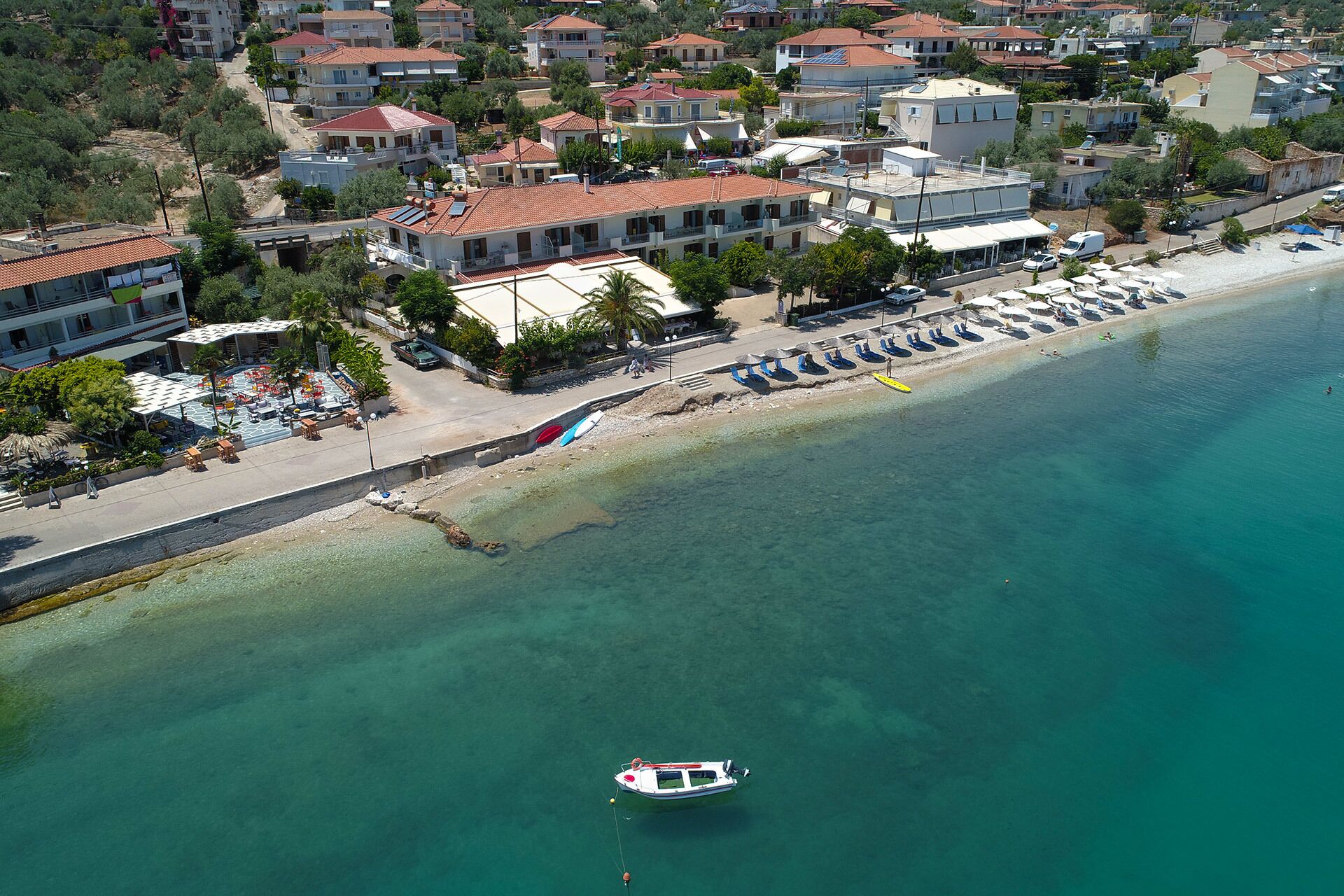 An aerial view of a coastal area with a beach, a row of beachside buildings, and a boat anchored near the shore.