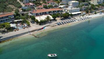 An aerial view of a coastal area with a beach, a row of beachside buildings, and a boat anchored near the shore.