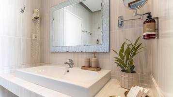 Een moderne badkamer met een groot wit wastafel, een spiegel met decoratieve lijst, een handdouche en een kamerplant.