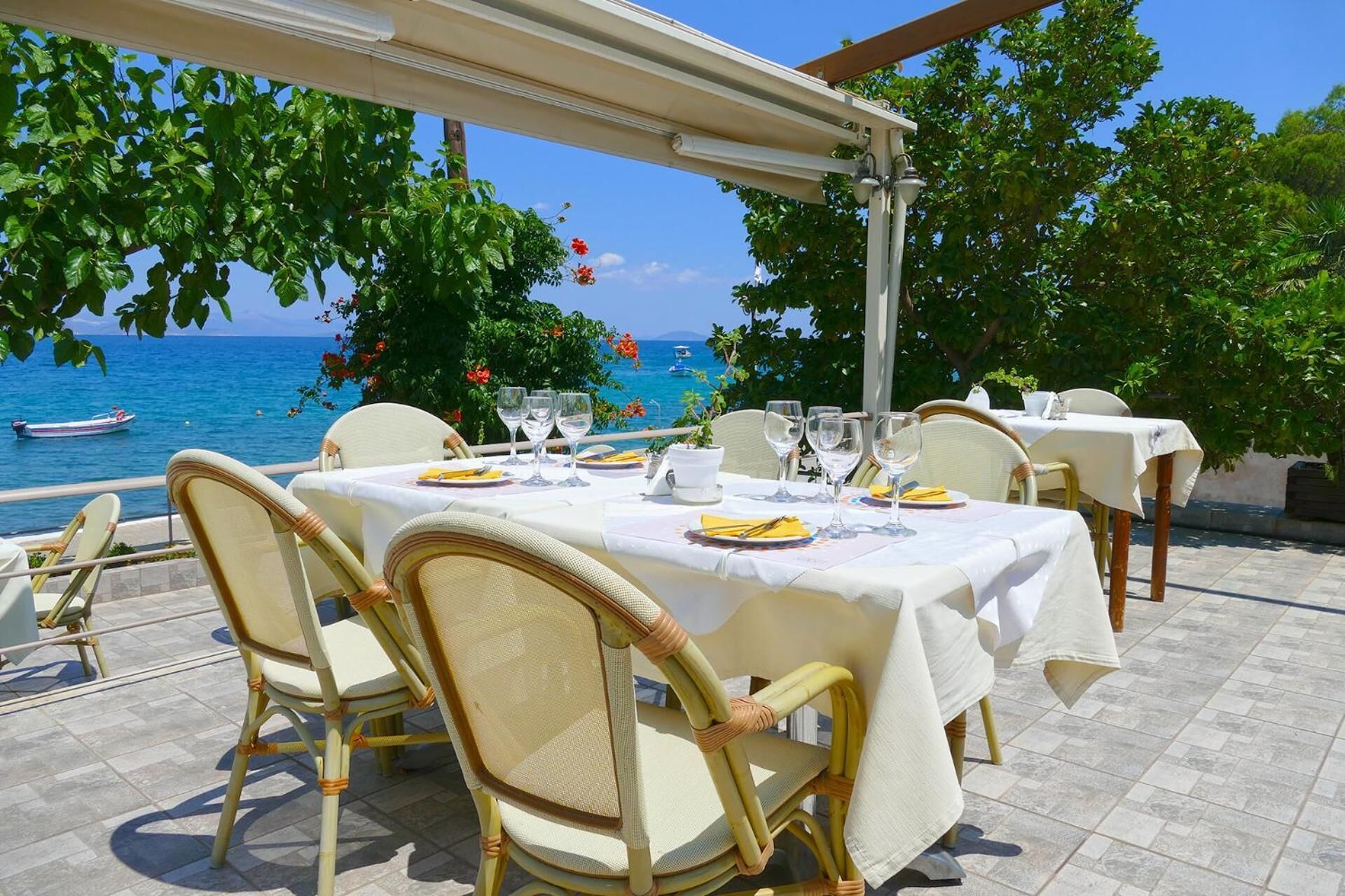 An outdoor dining area with tables set for two, overlooking a body of water with boats.