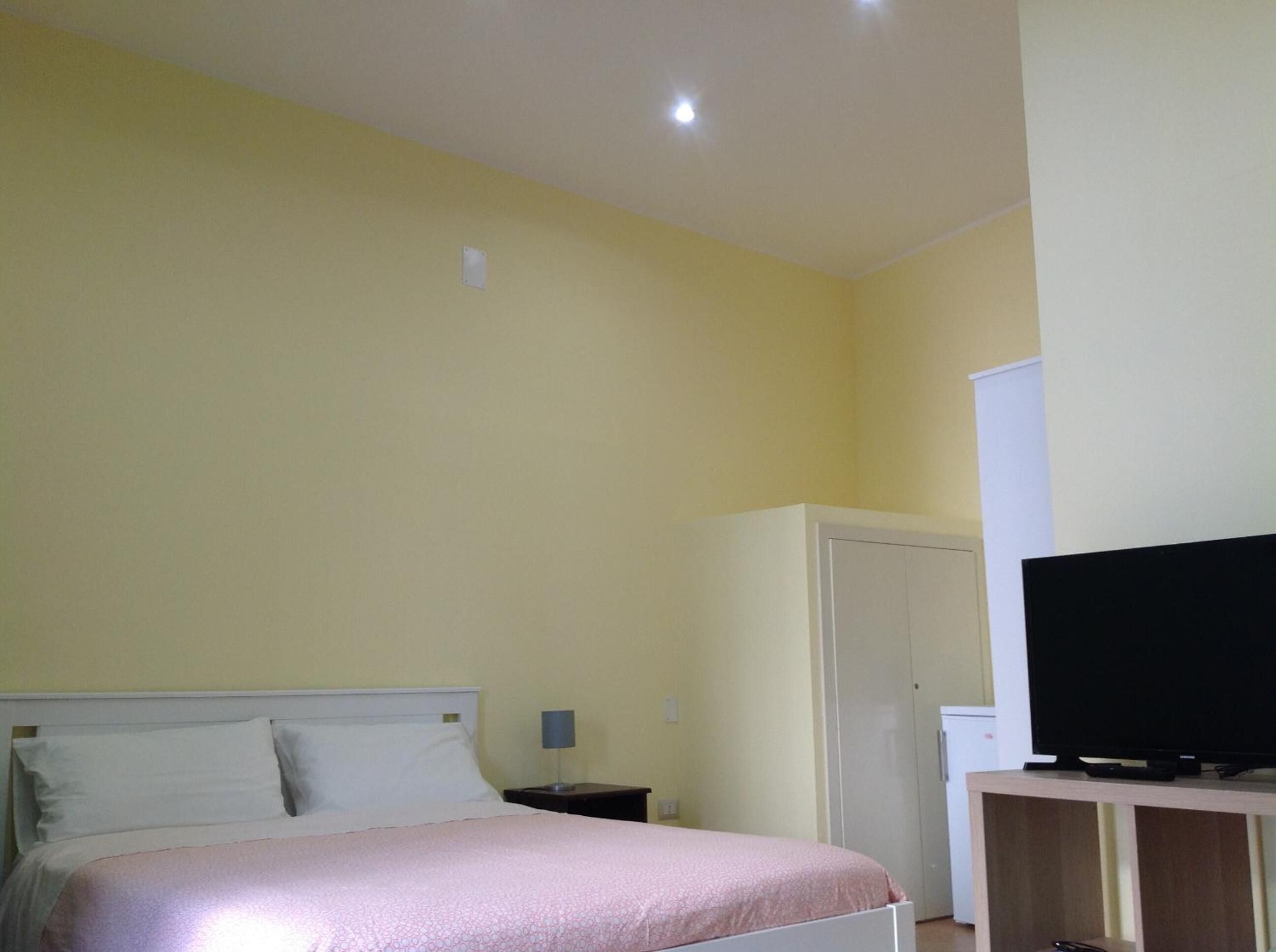 A bedroom with a bed, a nightstand, a television on a stand, and a wardrobe.