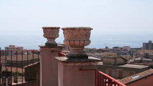 A balcony with ornate stone balustrades overlooking a coastal cityscape.
