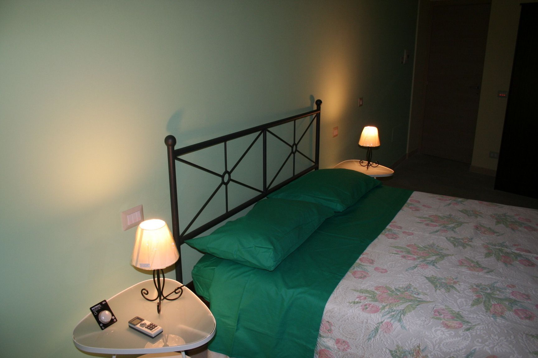 A neatly made bed with a green pillow and a floral bedspread, flanked by two bedside tables with lamps and a small clock.