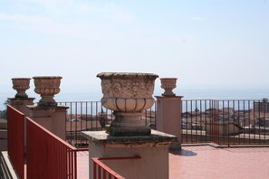 Un balcon orné de vases en pierre et doté d’une balustrade rouge, d’où l’on peut admirer une vue panoramique sur la ville côtière.