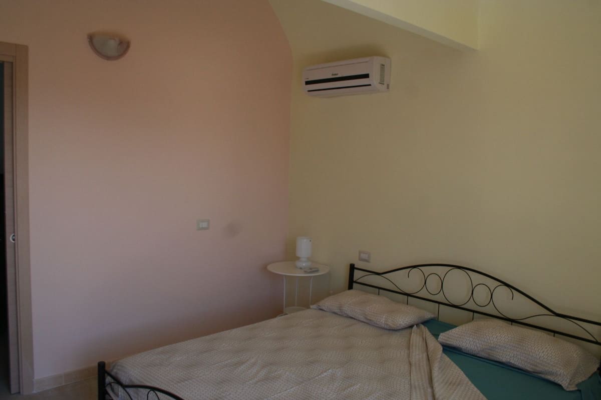 Une chambre à coucher comprenant un lit, une table de chevet, un climatiseur et un luminaire fixé au mur.