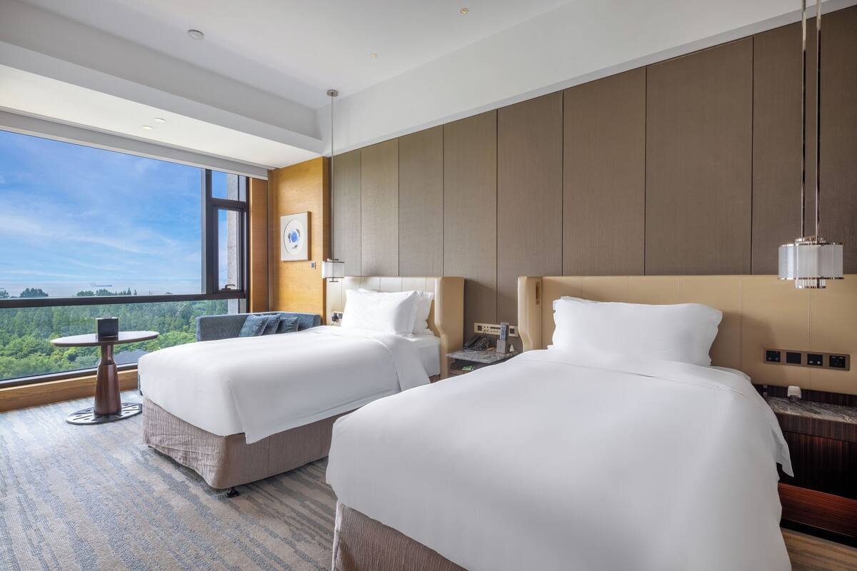 Een hotelkamer met twee bedden, een tafeltje en uitzicht op de omgeving.
