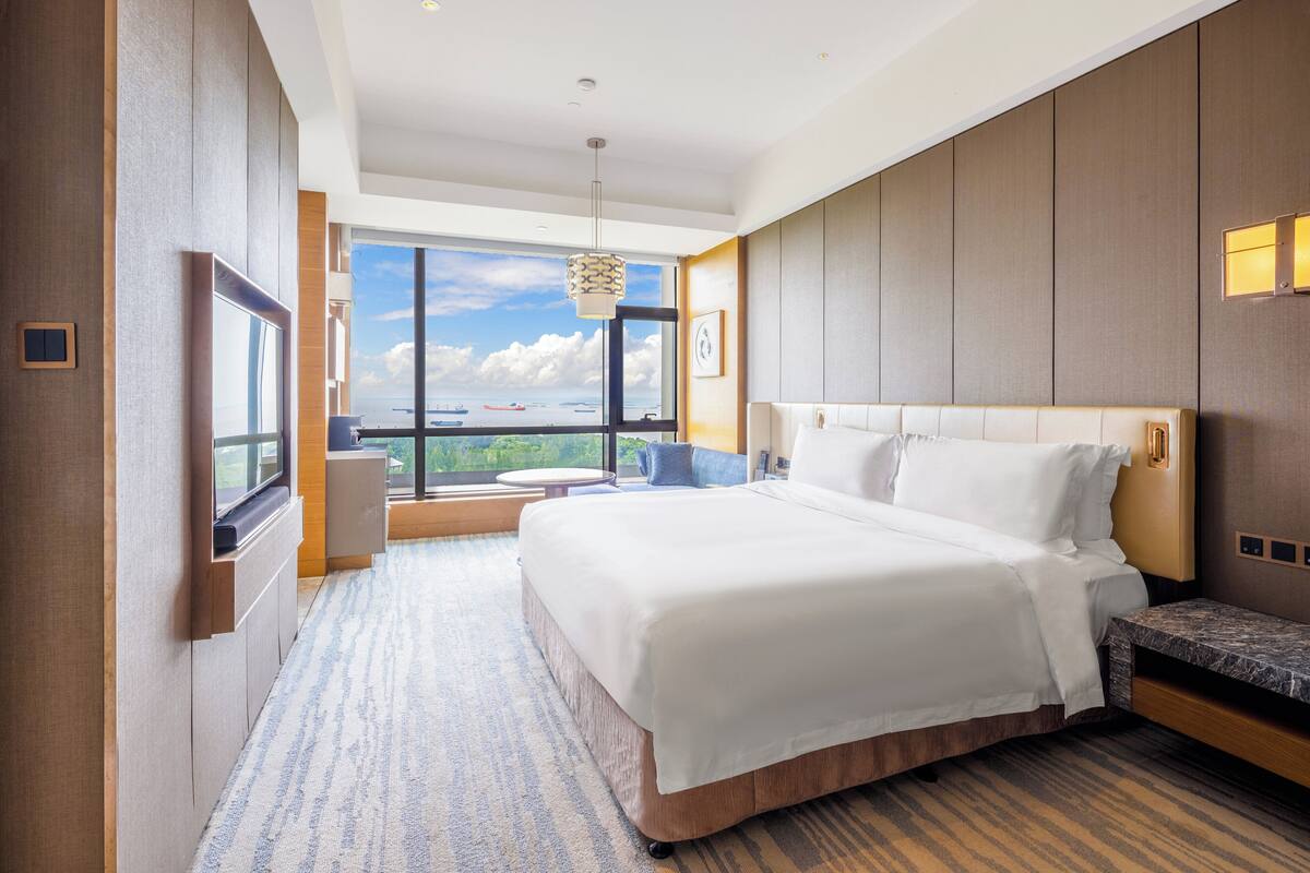 Een moderne hotelkamer met een groot bed, uitzicht op de stad en een balkon met uitzicht op zee.