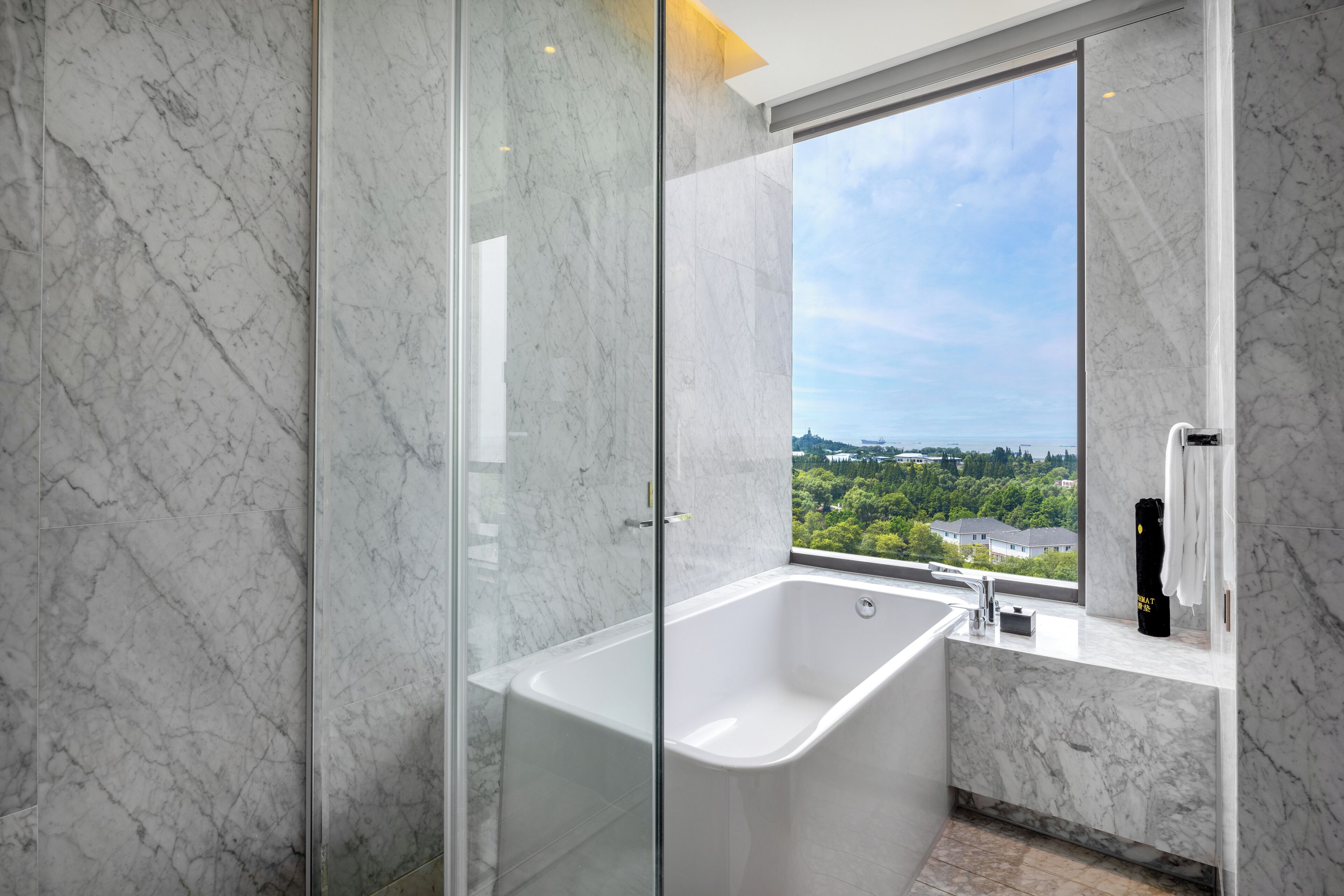 A modern bathroom with a glass-enclosed shower, a freestanding bathtub, and a window offering a city view.