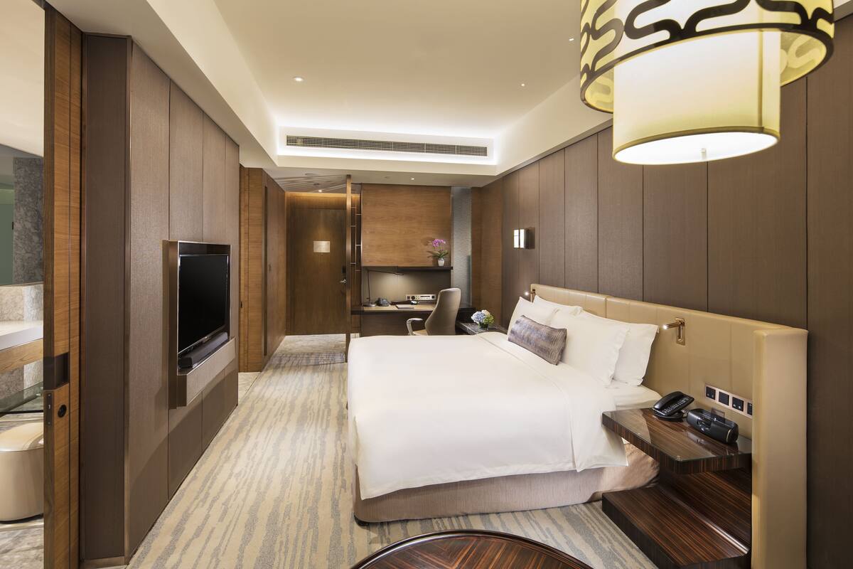 Een moderne hotelkamer met een groot bed, een bureau, een flatscreen televisie en een badkamer met een glazen scheiding.